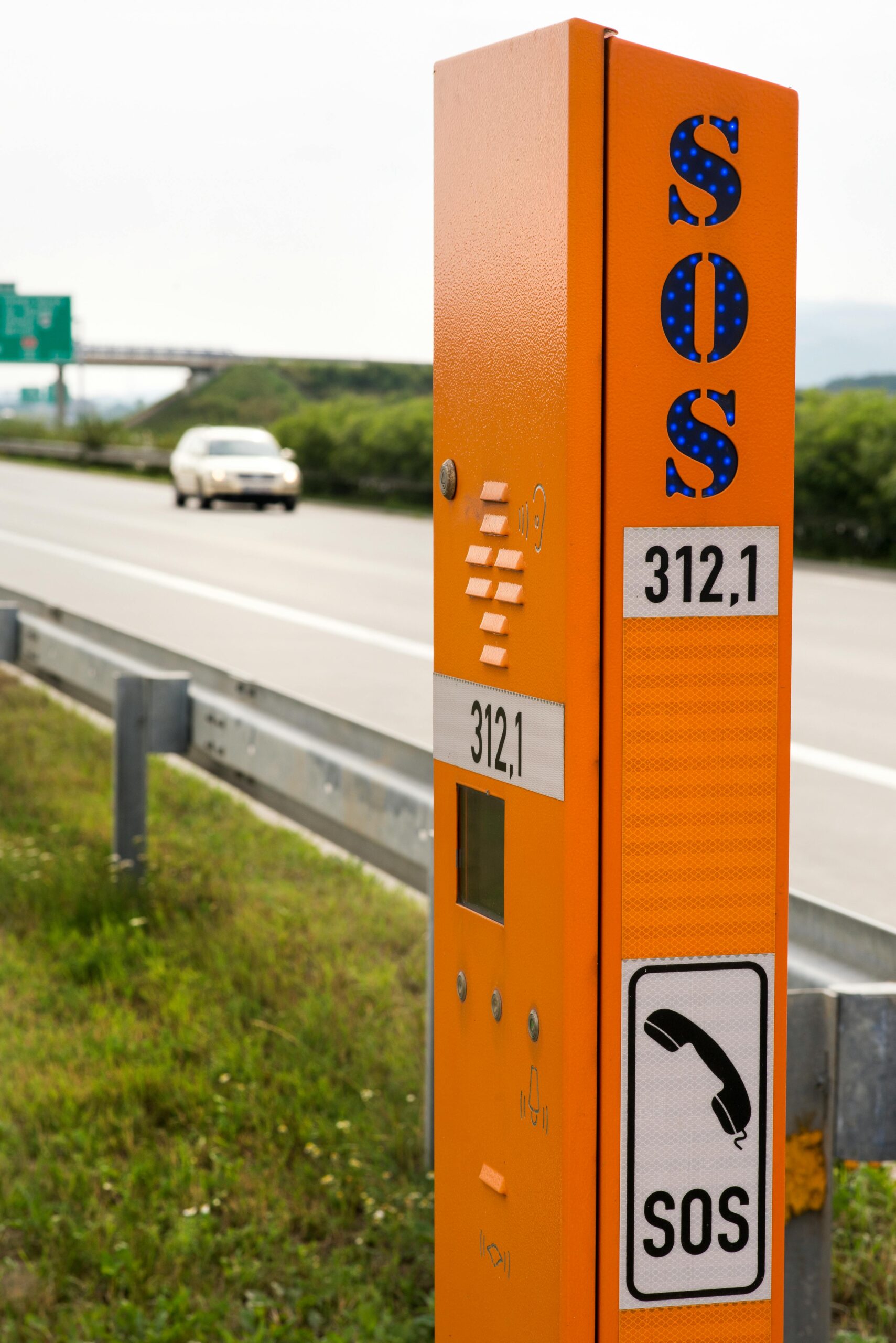 Orange SOS emergency phone on a highway with a blurred car in the background.
