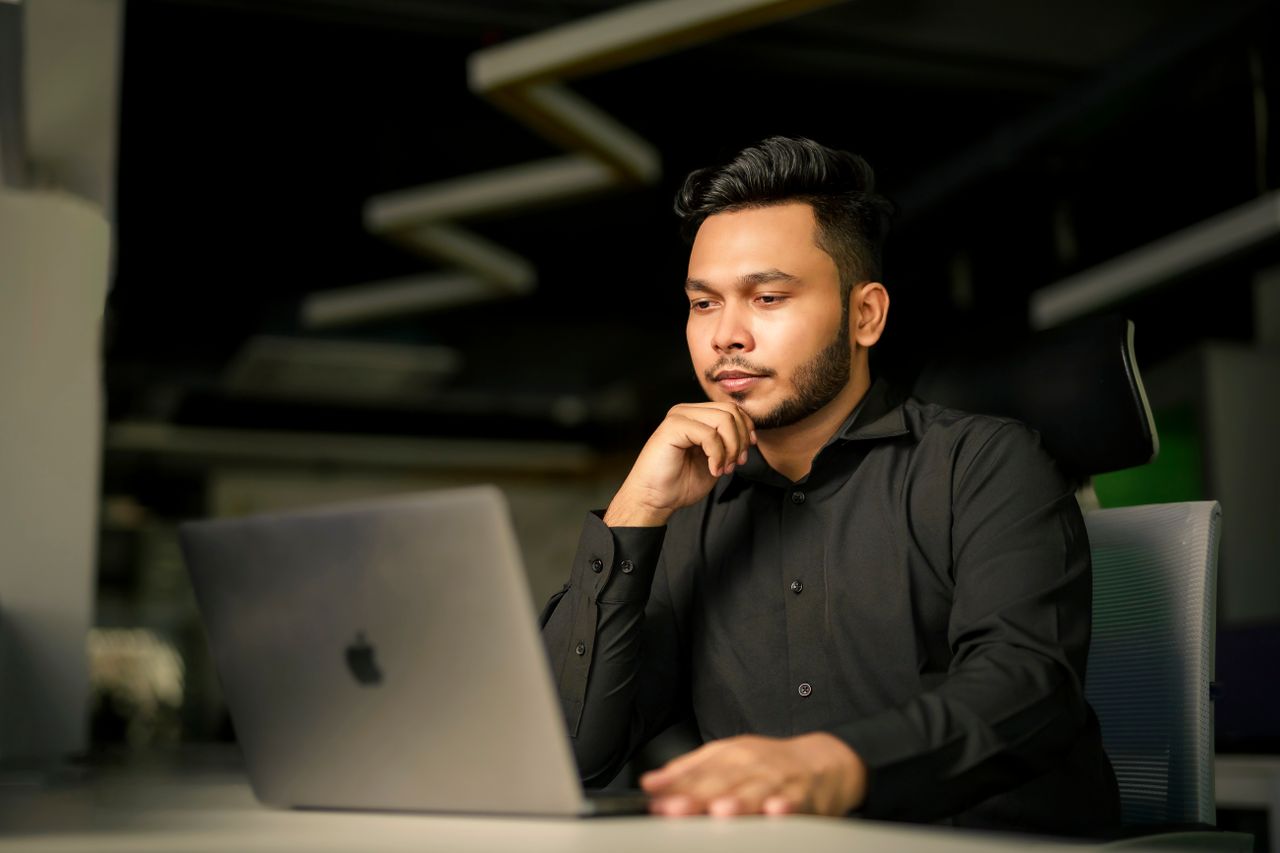 Home Young South Asian man in black shirt concentrating on work with laptop in modern office.