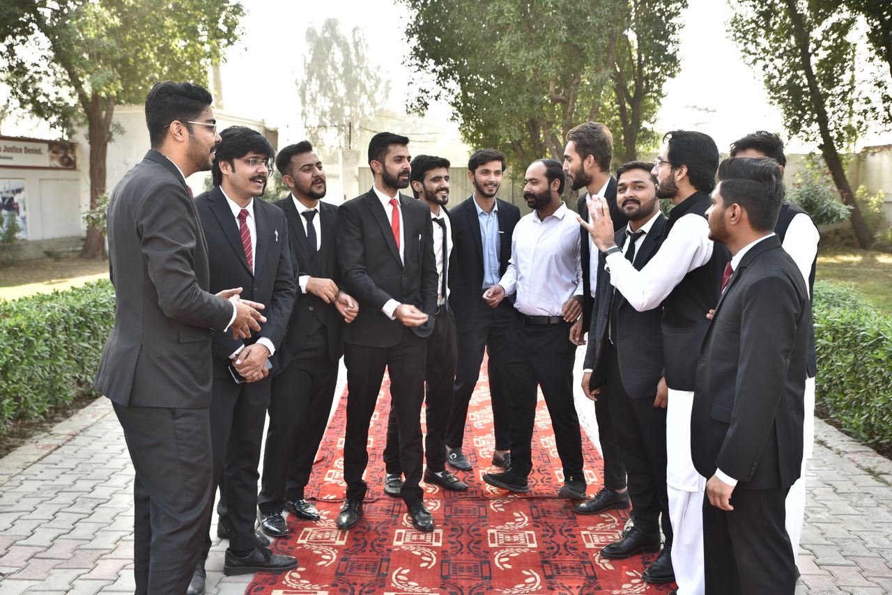 Home A group of men in formal attire conversing outdoors on a sunny day.